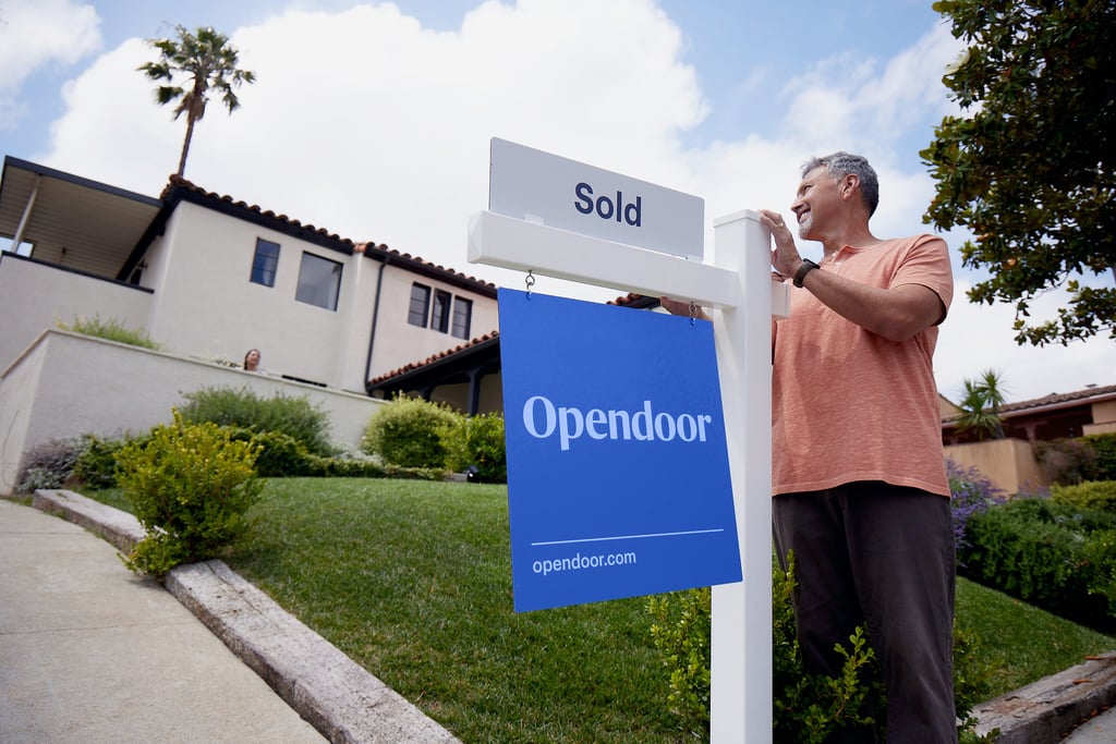 A man standing new to an Opendoor "Sold" sign and looking satisfied.