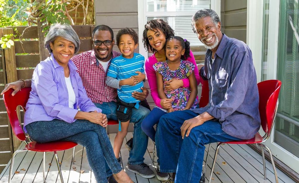 A family gathered on the front porch of a two-story suburban home at dusk.