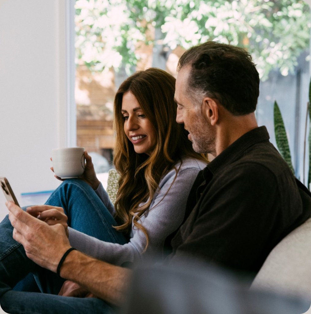 Two people sitting on a sofa looking at a phone together