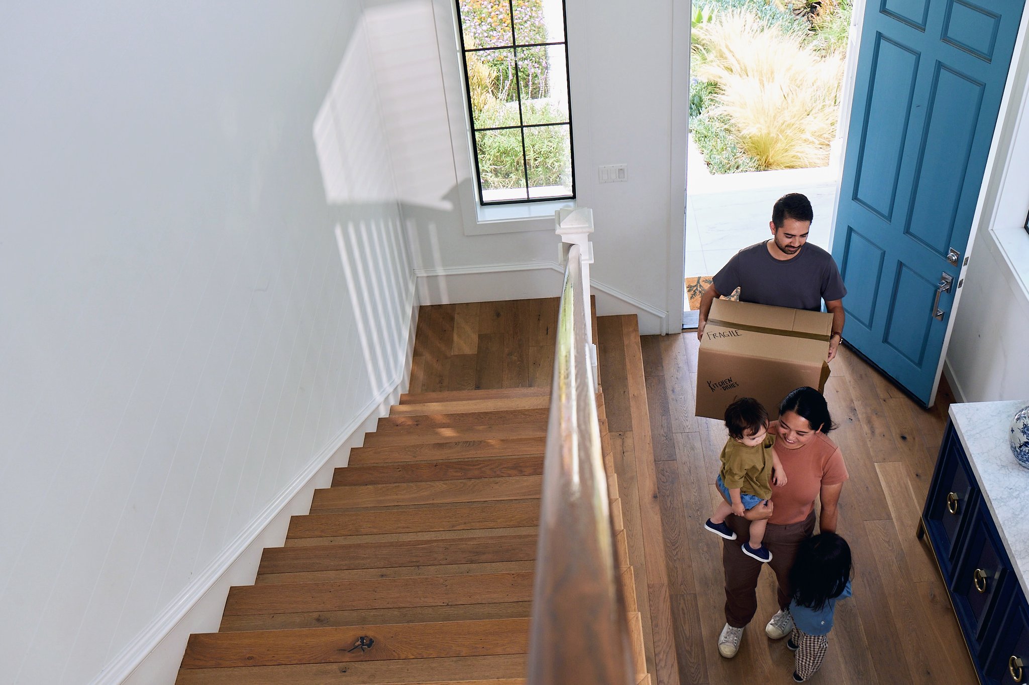 Couple carrying moving boxes into a sunny home hallway